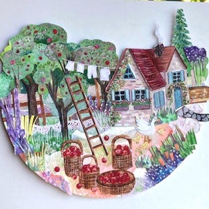 May include: A layered paper collage illustration depicting a cottage with a red roof, a wooden ladder, and apple trees. Baskets filled with red apples sit on the ground near a white goose and chicks. A clothesline with white laundry hangs nearby.