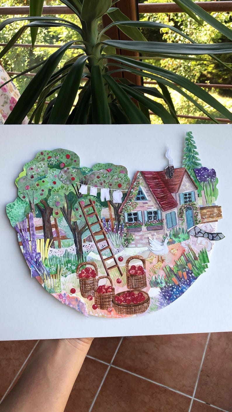 May include: A layered paper collage illustration depicting a cottage with a red roof, a wooden ladder, and apple trees. Three woven baskets filled with red apples sit on the ground near a white goose and chicks, with laundry hanging on a line.