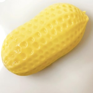 May include: A bright yellow, oblong-shaped object with a textured, dimpled surface that mimics the appearance of a peanut shell. The item has a smooth, glossy finish and a rounded, symmetrical form, appearing as a single, solid, moulded piece.