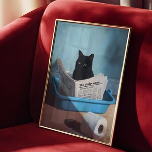May include: A framed print featuring a black cat sitting in a blue litter box, reading a newspaper titled "The daily news." A roll of toilet paper is on the floor. The frame has a gold finish, and the print is set against a red velvet background.