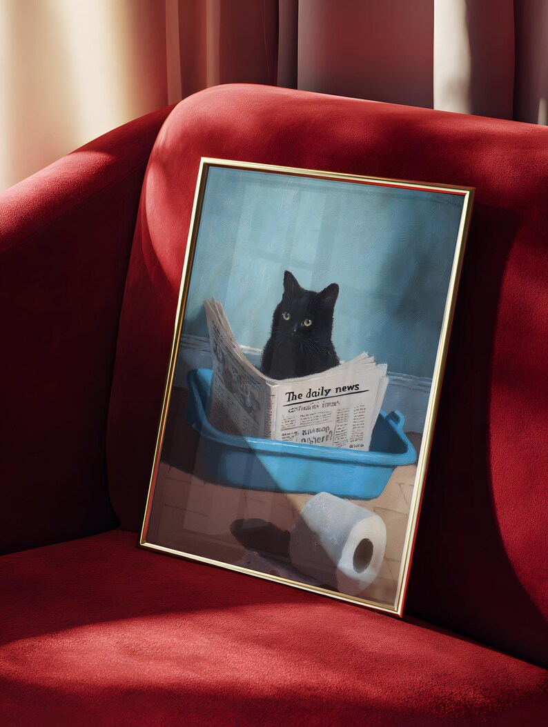 May include: A framed print featuring a black cat sitting in a blue litter box, reading a newspaper titled "The daily news." A roll of toilet paper is on the floor. The frame has a gold finish, and the print is set against a red velvet background.