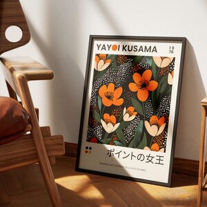 K&ouml;nnte beinhalten: Ein schwarzer gerahmter Poster mit einem floralen Design mit orangefarbenen Blumen auf schwarzem Hintergrund mit wei&szlig;en Punkten. Der Poster tr&auml;gt den Text "Yayoi Kusama" und "ポイントの女王" in Japanisch.