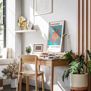 May include: A wooden desk with a chair, a lamp, and a poster featuring a turtle with the text "Yayoi Kusama" and "水玉の女王" in Japanese. There are plants in pots and a shelf with decorative items on the wall.
