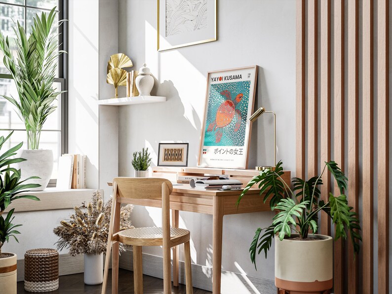May include: A wooden desk with a chair, a lamp, and a poster featuring a turtle with the text "Yayoi Kusama" and "水玉の女王" in Japanese. There are plants in pots and a shelf with decorative items on the wall.