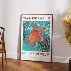 May include: A framed poster with a colorful illustration of a sea turtle on a blue background with white dots. The poster is titled "Yayoi Kusama 1977" and features the text "ポイントの女王" in Japanese. The poster is framed in a brown wood frame.