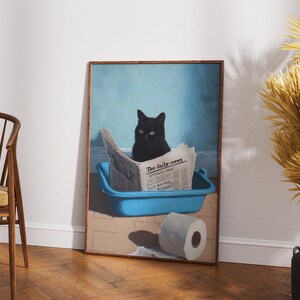 May include: A framed print depicts a black cat sitting in a blue litter box, reading a newspaper titled "The Daily News." A roll of toilet paper sits on the floor. The background is a light blue wall.