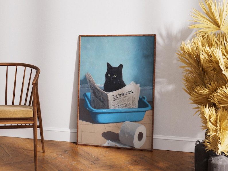 May include: A framed print depicts a black cat sitting in a blue litter box, reading a newspaper titled "The Daily News." A roll of toilet paper sits on the floor. The background is a light blue wall.