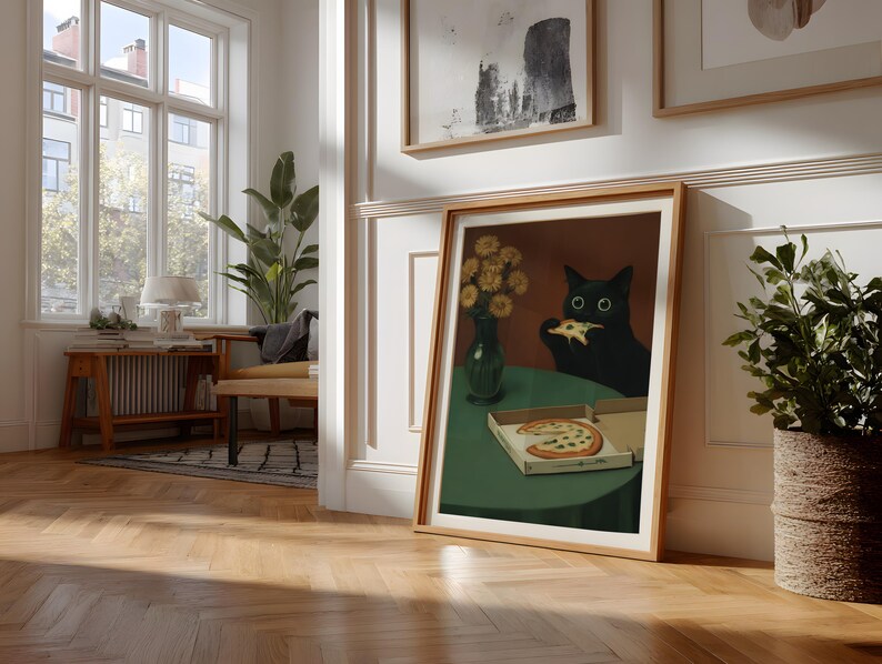 May include: A framed art print depicts a black cat eating pizza at a green table. A vase of yellow flowers sits on the table. A pizza box with a slice of pizza is also on the table. The artwork is in a room with a window and wooden floors.