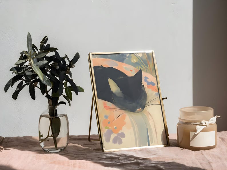Puede incluir: Una imagen enmarcada en oro de un gato negro durmiendo sobre un fondo colorido con estampado floral. La imagen est&aacute; sobre un caballete dorado y se encuentra sobre una mesa rosa.