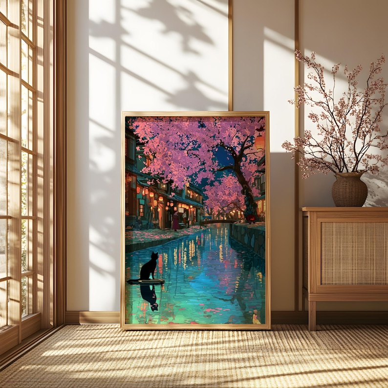 May include: A framed art print depicts a nighttime scene of a Japanese canal lined with buildings and illuminated by lanterns. Pink cherry blossoms overhang the water, reflecting the lights. A black cat sits on a small platform in the water.