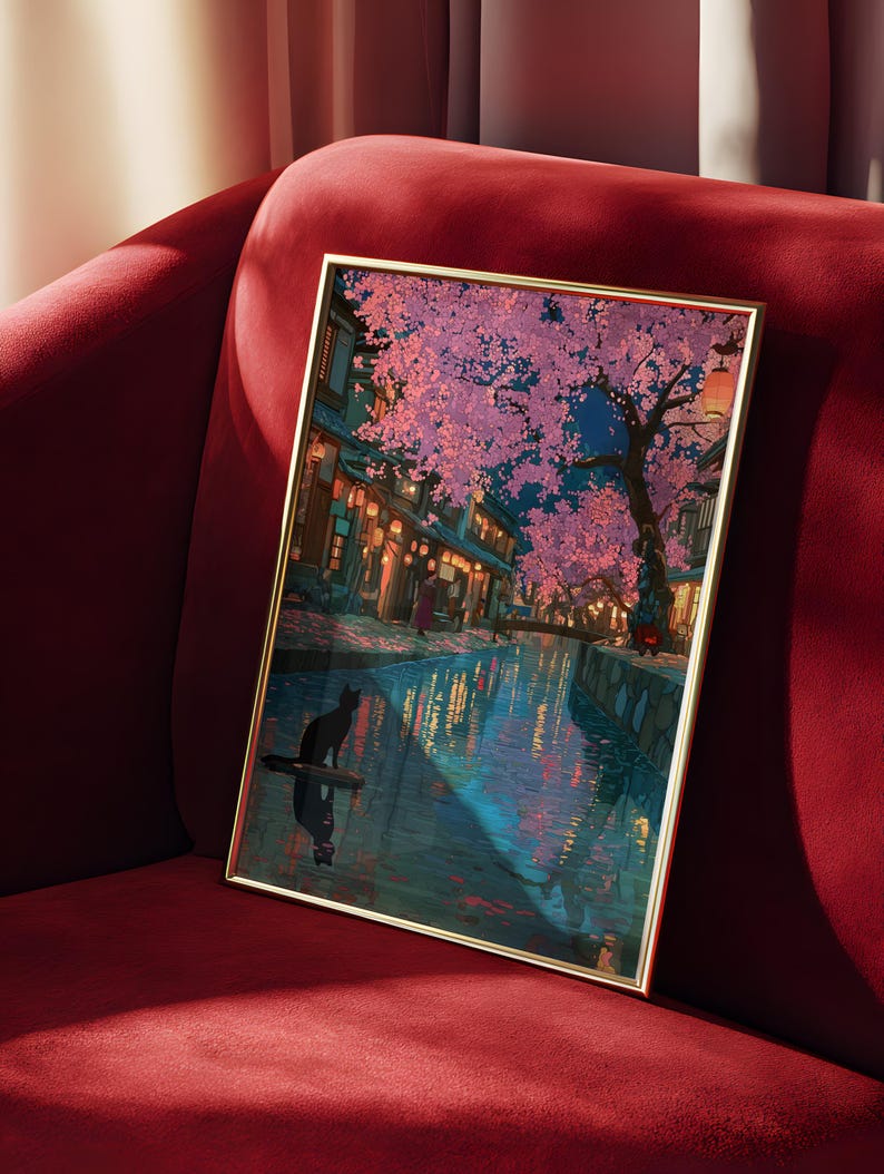 May include: Framed art print depicting a nighttime scene with a canal, cherry blossom trees, and traditional buildings. A black cat is silhouetted on a floating object in the water. The artwork has a gold frame and is displayed on a red velvet surface.
