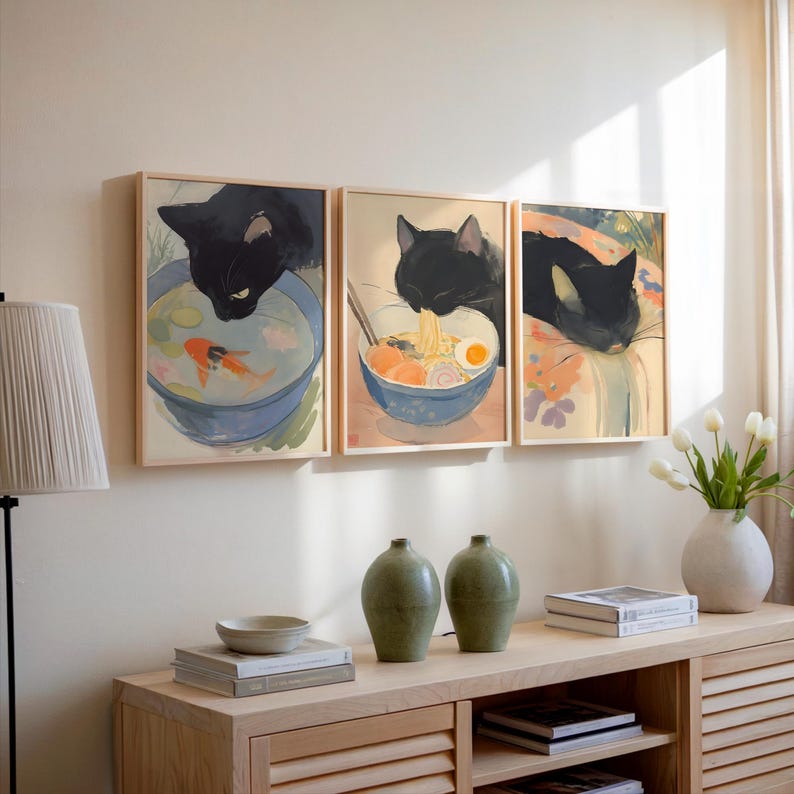 Puede incluir: Tres ilustraciones enmarcadas de gatos negros. La primera muestra un gato mirando un cuenco de agua con un pez dorado. La segunda muestra un gato comiendo fideos ramen de un cuenco. La tercera muestra un gato durmiendo en una manta.