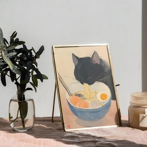 Puede incluir: Una imagen enmarcada en oro de un gato negro comiendo fideos ramen de un taz&oacute;n azul. La imagen est&aacute; en un caballete de madera y hay una vela en el fondo.