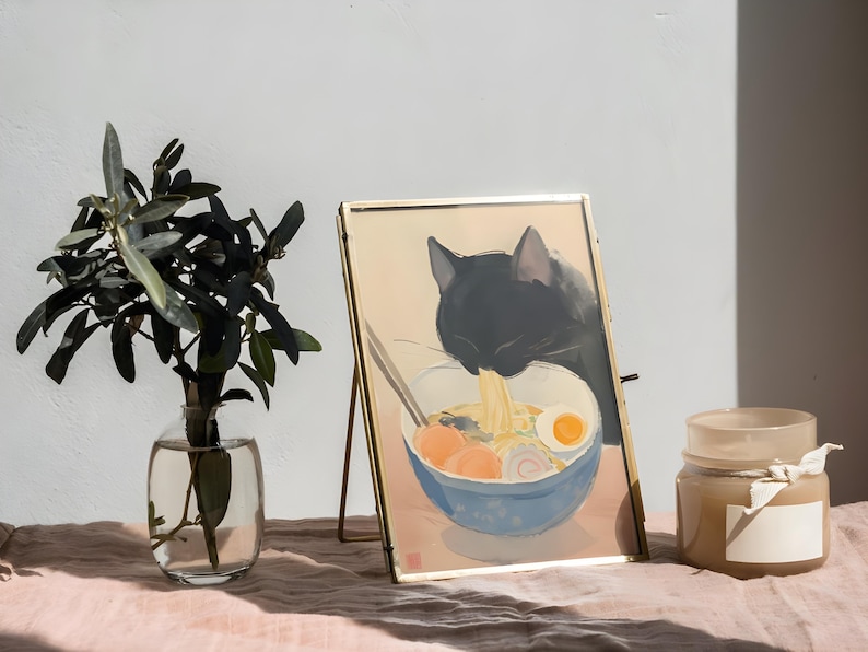 Puede incluir: Una imagen enmarcada en oro de un gato negro comiendo fideos ramen de un taz&oacute;n azul. La imagen est&aacute; en un caballete de madera y hay una vela en el fondo.