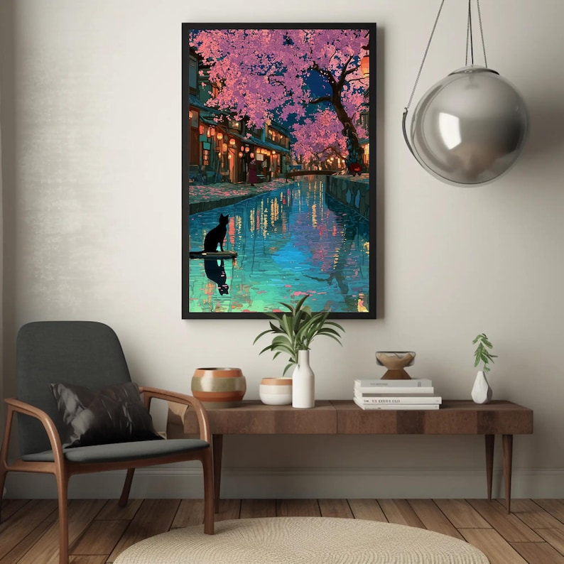 May include: A framed art print depicts a serene canal scene at dusk. Cherry blossoms in shades of pink and purple frame the buildings and water. A black cat sits on a small platform, reflected in the water.