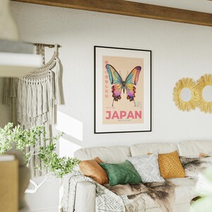 May include: A framed poster with a colorful butterfly illustration and the word "JAPAN" in pink letters. The poster is hanging on a white wall above a couch with pillows and a throw blanket.
