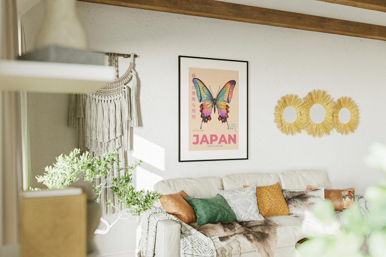 May include: A framed poster with a colorful butterfly illustration and the word "JAPAN" in pink letters. The poster is hanging on a white wall above a couch with pillows and a throw blanket.