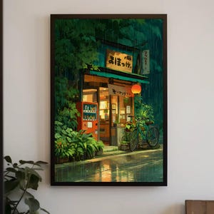 Op de afbeelding: Ingelijste kunstdruk van een Japanse winkel in de regen. De winkel heeft een rode automaat, een fiets en een oranje lantaarn. Weelderig groen gebladerte omringt de winkel en de straat weerspiegelt de regen.