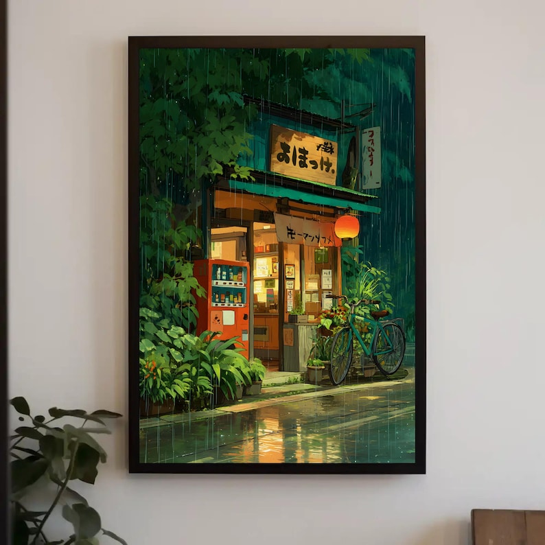 Op de afbeelding: Ingelijste kunstdruk van een Japanse winkel in de regen. De winkel heeft een rode automaat, een fiets en een oranje lantaarn. Weelderig groen gebladerte omringt de winkel en de straat weerspiegelt de regen.