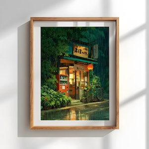 Op de afbeelding: Ingelijste kunstdruk van een Japanse straatsc&egrave;ne in de regen. Een kleine winkel met een rode automaat en een fiets zijn zichtbaar. De winkel heeft een groen dak en een rode lantaarn. Weelderig groen gebladerte omringt de winkel.
