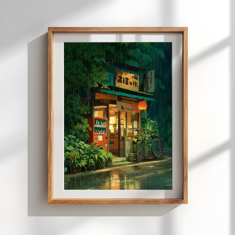 Op de afbeelding: Ingelijste kunstdruk van een Japanse straatsc&egrave;ne in de regen. Een kleine winkel met een rode automaat en een fiets zijn zichtbaar. De winkel heeft een groen dak en een rode lantaarn. Weelderig groen gebladerte omringt de winkel.