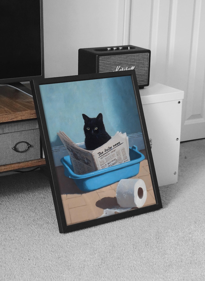May include: Framed art print featuring a black cat sitting in a blue litter box, reading a newspaper titled "The Daily News". A roll of toilet paper sits nearby. The background is a light blue wall.