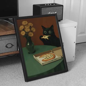 May include: Framed art print featuring a black cat eating pizza. The cat is depicted with large green eyes, sitting at a green table with a pizza box and a vase of yellow flowers. The background is a warm brown.
