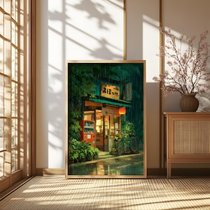 Op de afbeelding: Een ingelijste print van een Japanse straatsc&egrave;ne. Het kunstwerk toont een kleine winkel met een rode automaat, een fiets en een gloeiende lantaarn. Het bord van de winkel heeft Japanse tekst. De sc&egrave;ne speelt zich af in de regen.