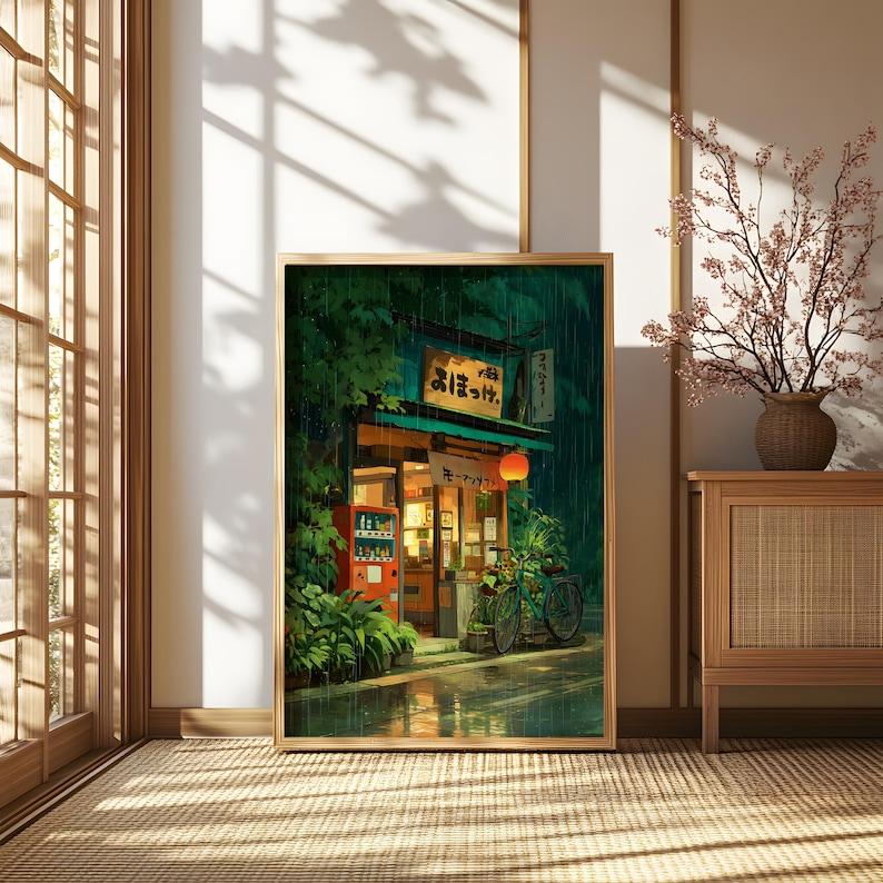 Op de afbeelding: Een ingelijste print van een Japanse straatsc&egrave;ne. Het kunstwerk toont een kleine winkel met een rode automaat, een fiets en een gloeiende lantaarn. Het bord van de winkel heeft Japanse tekst. De sc&egrave;ne speelt zich af in de regen.