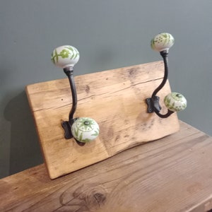 May include: Two hooks with green and white ceramic knobs mounted on a rustic wooden board. The board is made of reclaimed wood and has a natural finish.