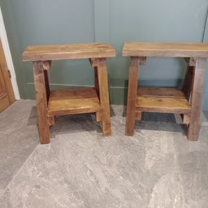 Puede incluir: Dos mesas auxiliares de madera con un acabado rústico marrón. Las mesas tienen un diseño sencillo con dos estantes y una tapa rectangular.