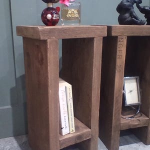 May include: Two rustic, wooden side tables with a natural finish. Each table has a shelf and is decorated with items like books, perfume bottles, and a small clock. One table has the text "INGER 22" on the side.