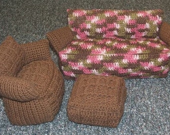 May include: A crocheted dollhouse furniture set featuring a brown armchair, a small brown ottoman, and a sofa with a patterned cushion in shades of pink, green, and brown. The set is designed for a dollhouse.