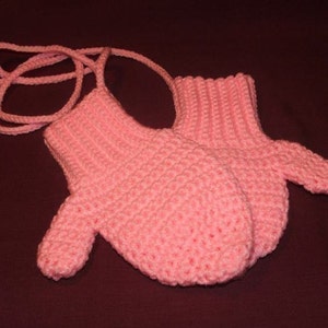May include: A pair of pink crocheted mittens with a matching pink crocheted string attached.