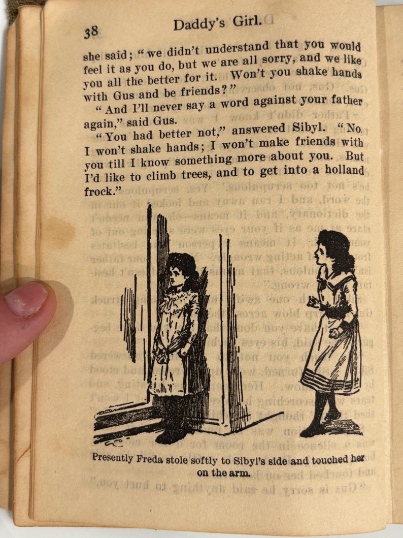K&ouml;nnte beinhalten: Schwarz-wei&szlig;-Illustration von zwei M&auml;dchen, die in einem T&uuml;rrahmen stehen. Das M&auml;dchen links tr&auml;gt ein langes Kleid und das M&auml;dchen rechts tr&auml;gt ein Kleid mit Matrosenkragen. Der Text "Presently Freda stole softly to Sibyl's side and touched her on the arm." ist unter der Illustration gedruckt.