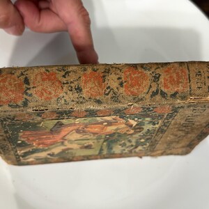 K&ouml;nnte beinhalten: Ein altes Buch mit einem abgenutzten braunen Einband und einer verblassten Illustration einer Frau in einem roten Kleid. Der Buchr&uuml;cken hat japanischen Text und die Worte "Die kleine rote Henne" stehen auf dem Einband.
