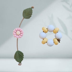 Könnte beinhalten: Eine rosa Blume mit grünen Blättern und einem weißen und gelben Perlenarmband.