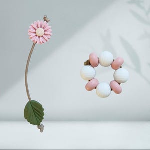 May include: A pink flower with a white centre attached to a brown string with a green leaf. A pink and white beaded bracelet with a brown string.