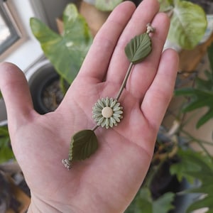 May include: A green and white flower charm with green leaves on a string. The charm is made of polymer clay and is handmade.