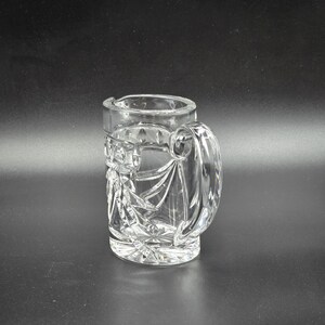 May include: A clear glass pitcher with a cut glass design. The pitcher has a handle and a wide mouth.