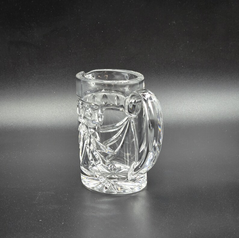 May include: A clear glass pitcher with a cut glass design. The pitcher has a handle and a wide mouth.