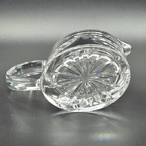 May include: A clear glass pitcher with a cut glass design. The pitcher has a round body and a handle.
