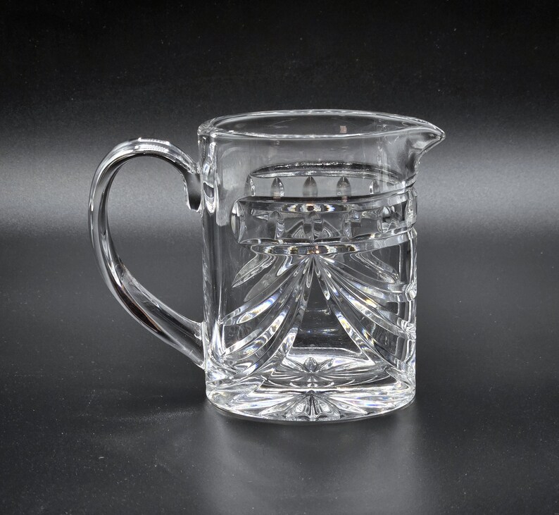 May include: A clear glass pitcher with a cut glass design. The pitcher has a handle and a spout.