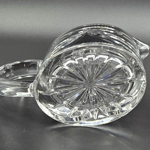 May include: A clear glass pitcher with a cut glass design. The pitcher has a handle and a spout.