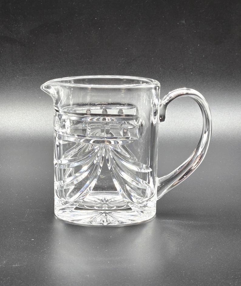 May include: A clear glass pitcher with a cut glass design. The pitcher has a handle and a wide mouth.