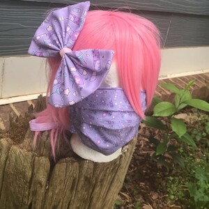 May include: A purple face mask with a pattern of syringes, bandages, and pills. The mask is worn by a mannequin with pink hair and a purple bow with the same pattern as the mask.