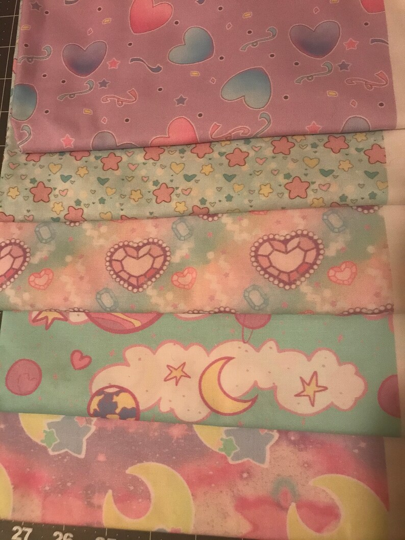 May include: Five different fabric swatches with pastel pink, blue, and green colors. The fabrics feature various patterns including hearts, stars, moons, and clouds.