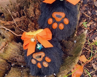 May include: Two black furry paw-shaped keychains with orange paw prints and a small orange bow with a gold bell charm.