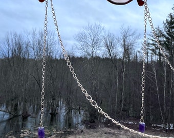 May include: Round pink tinted glasses with a silver chain attached to each side. The chain has a purple crystal at the end.