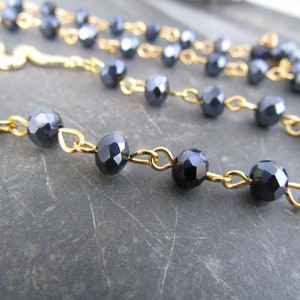 May include: A gold chain necklace with black faceted beads. The chain is made of small, delicate links.